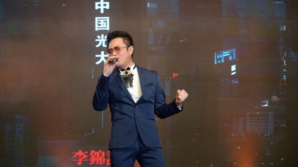 A person in a suit singing into a microphoneDescription automatically generated